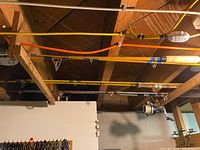 Photo showing multiple fishing rods mounted horizontally with wooden bracing in a storage area. Rods are in different colors, mostly yellow and one orange, with one rod having a white reel attached.