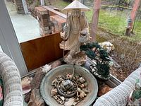 Full view of carved stone statue, basin, bonsai tree and surrounding shells and stones