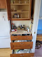 Kitchen shelving with various glassware, brass teapot on counter, pens and other small items on countertop, open drawers with kitchen utensils and plates visible.