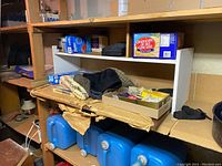 Photo of wooden shelving with blue plastic water carriers, cardboard boxes, and various small items including knit hats and kitchen goods