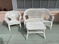Photo of the entire furniture set including white wicker armchair, loveseat, and coffee table on outdoor patio with visible wear on paint and wicker edges.