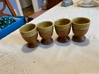 Four Mid Century egg cups with teakwood bases, arranged in a row on a white cloth surface showing overall set and condition.