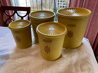 Set of 4 vintage yellow Tupperware canisters with lids, showing size differences and sunburst lid design on a table near window.