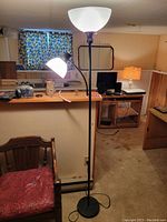 Full view of the standing floor lamp showing both the large upward-facing bowl-shaped frosted glass shade and the smaller adjustable side light with white frosted glass shade, dark metal pole and base, situated in a room.