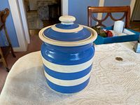 Front and side view of the blue and white striped ceramic container with lid on a table.