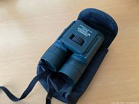 Trophy Waterproof binoculars in soft black pouch with strap on wood surface