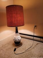 Full view of the lamp turned on with dark brown textured barrel shade.
