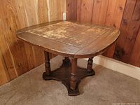 Full angled view of the vintage solid wood Art Deco-style square table showing the top surface wear and rounded edges with sculpted legs and base.