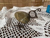 Photo of vintage bird sculpture showing side view with stone body and metal legs on crocheted cloth surface