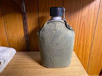 Front view of WWII-era water canteen with olive green fabric cover and black screw cap.