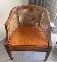 Front view of vintage cane back club chair showing orange velvet cushion and wood frame