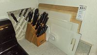 Photo shows a wooden knife block with multiple black-handled Farberware knives. To the side, there are wooden and plastic cutting boards in varied sizes.