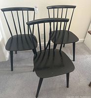 Three black painted Danish modern chairs grouped, showing full view of the chairs with spindle back and tapered legs.
