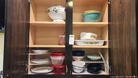 Two cupboard shelves filled with various kitchen dishes, bowls, and storage containers.