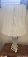 Full view of one glass table lamp with tall pleated white shade showing slight staining.