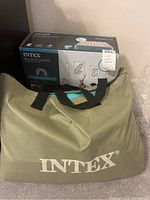 View of original box, Intex green carry bag with black straps, and wall background