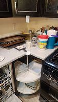 Photo of countertop with Pyrex glass baking dish, metal baking pans stacked, seasoning container, and various kitchen utensils in holder.