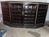 View of the front side of the black mid-century credenza showing patterned front panels and gold trim details.