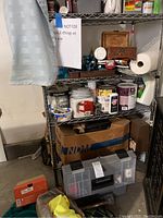 Wide shot of metal shelving with various paint cans, cleaning supplies, and a large tool box at the bottom.