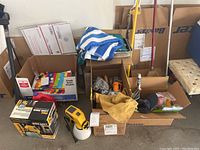 Lot overview showing boxes containing Wagner paint sprayer, hand tools, painting and cleaning supplies on concrete floor.