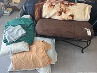 Overview of brown ultra suede cushioned bench with multiple bedding pieces stacked on and around it including pillowcases, sheets, and floral blanket.