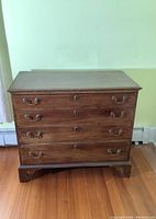 Front view of antique lowboy dresser showing four drawers with handles and keyholes, wood finish and simple bracket feet.