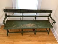 Full front view of the long, green painted wooden bench with curved armrests, showing overall condition and wear.