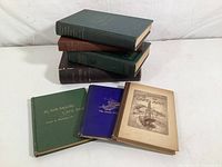Stack of seven historical books with different colored covers including green, purple, brown, tan, and blue showing front and back views.