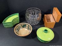 View of all 8 kitchen decor items: wooden recipe box, small floral stoneware bowl, large clear glass vase, four green pottery appetizer dishes and one covered bowl.