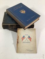 Four antique books stacked showing covers and condition, titles visible on blue hardcovers and softcover with American flags.