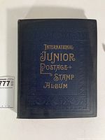 Front cover of navy cloth-bound album embossed with gold lettering 'International Junior Postage + Stamp Album'