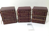 Photo of 33 volumes of The Temple Shakespeare series stacked in three piles, showing titles on spines with red leather covers and gold embossing.