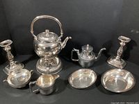 Full set showing two silver dishes, pair of candle holders, two coffee pots and creamer and sugar bowl on black background.