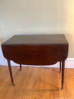 Front view of vintage drop leaf table with both leaves down showing overall shape and caster wheels