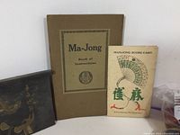 Photo showing Ma-Jong instruction book, score card, and painted wooden lid from original box.
