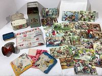 Overview photo showing three match tins, wooden stamps with numbers, fabric language guide, about 25 cat postcards, and four scarves with Disney prints.