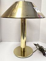 Front and side view of the brass table lamp showing the flared shade and cylindrical base with attached electrical cord and switch.
