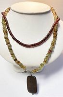 Display of two necklaces on a white bust: the longer jade and wood pendant necklace and shorter glass beaded choker