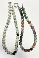 Two vintage jade beaded choker necklaces laid flat on a white background. One necklace features white jade with black speckles beads and gold-tone spacers; the other features multi-colored jade beads.