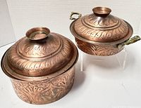 Photo showing both vintage repousse copper/brass covered pots with embossed floral patterns, highlighting lids and handles