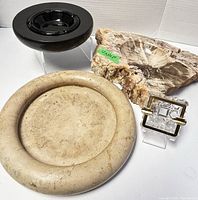 Five assorted ashtrays arranged on a white surface, showcasing variety of materials and sizes. Large natural stone ashtray visible with green size tag, alongside beige marble and small crystal ashtrays.