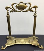 Front view of antique brass Art Nouveau style stand with curved feet and ornate top handle, patina visible.
