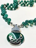 Close-up of green jade pendant with silver crown overlay and bail, attached to green jade bead necklace