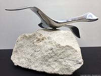 Front angle of chrome Canada Goose sculpture on stone base showing smooth metallic bird and textured base.