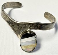 View of the front of the silver cuff bangle showing the oval abalone shell inlay with multicolored stripes and the textured tarnished silver band.