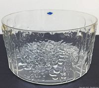 Side view of clear glass bowl showing embossed floral texture and blue Nuutajärvi Finland sticker near rim.