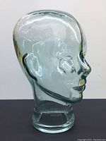 Front–right side view of transparent glass head showing molded facial features.