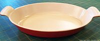 Top view of the oval Le Creuset baking dish showing white enamel interior and red handles with ridges.
