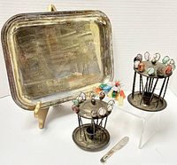 Photo of the large silver-tone serving tray propped on a stand next to two twisted metal pick holders topped with various colorful semi-precious stone picks, and a small spreader knife.