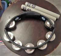 LP tambourine placed on a dark wooden surface with two white plastic King Klaves on top, showing tambourine's metal jingles and black frame with grip.